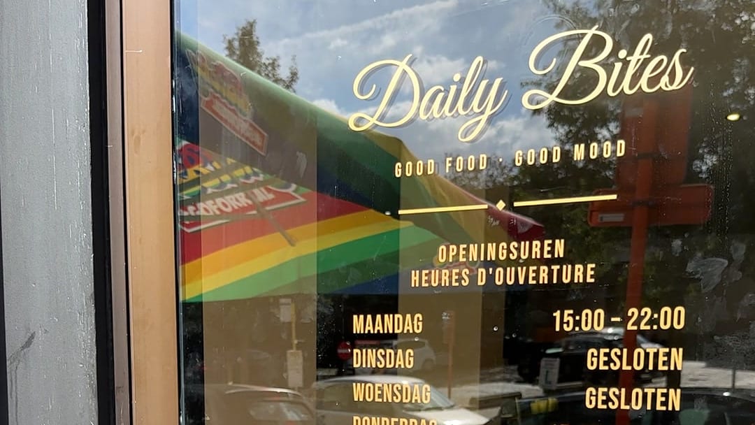 Eingangstür von Daily Bites in Voeren (Belgien): auf dem Glas der goldene Schriftzug «Daily Bites», «Good Food · Good Mood» und die Öffnungszeiten auf Niederländisch und Französisch